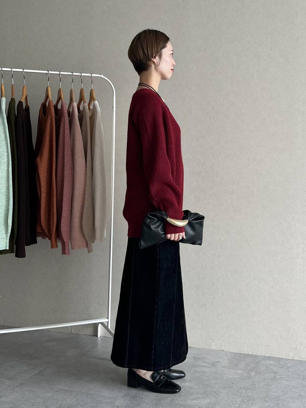 ブラック系のハンドバッグ、ブラック系のスカート、レッド系のニット/セーターを着用したレディースの秋コーディネートの2枚目の写真