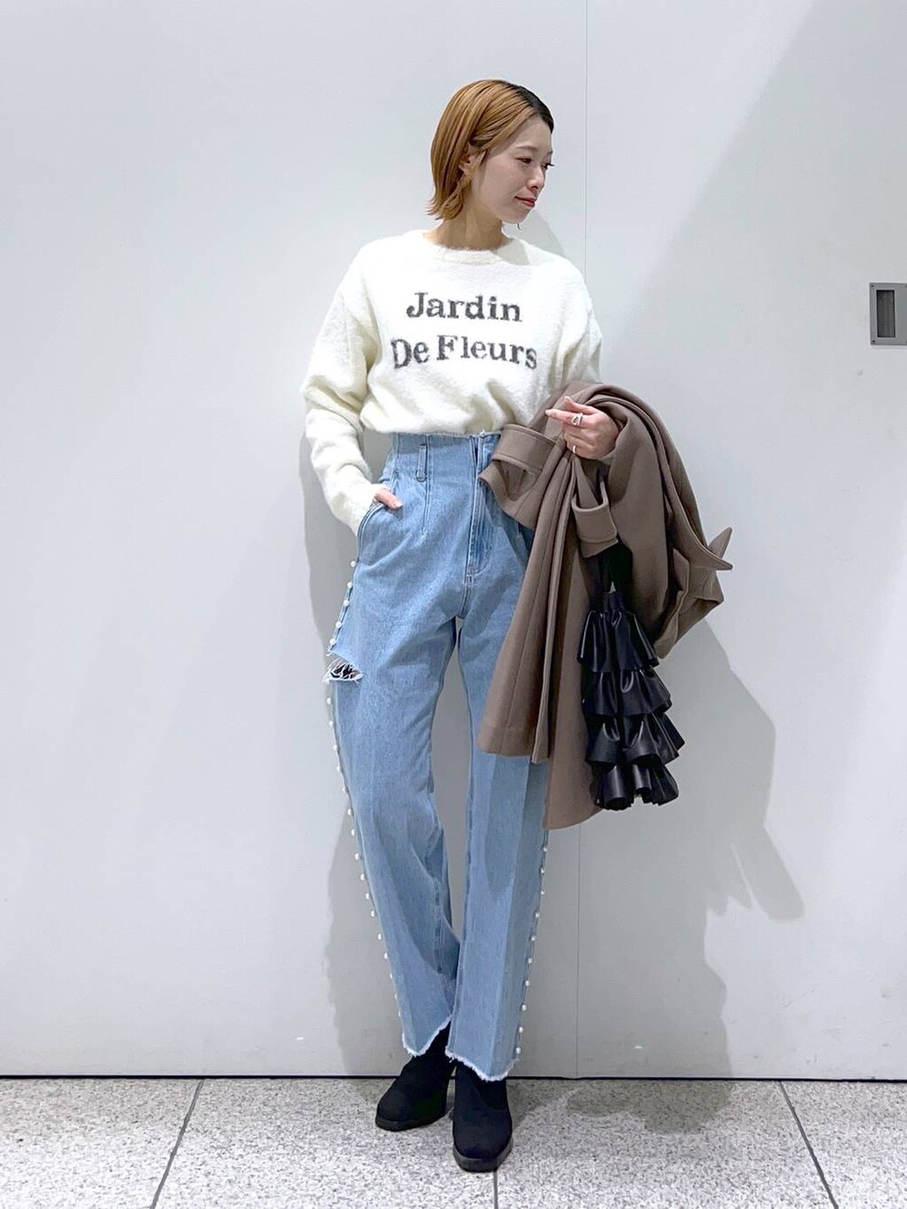 ホワイト系のニット/セーター、ブラウン系のチェスターコート、ブラック系のブーツを着用したレディースの冬コーディネートの4枚目の写真