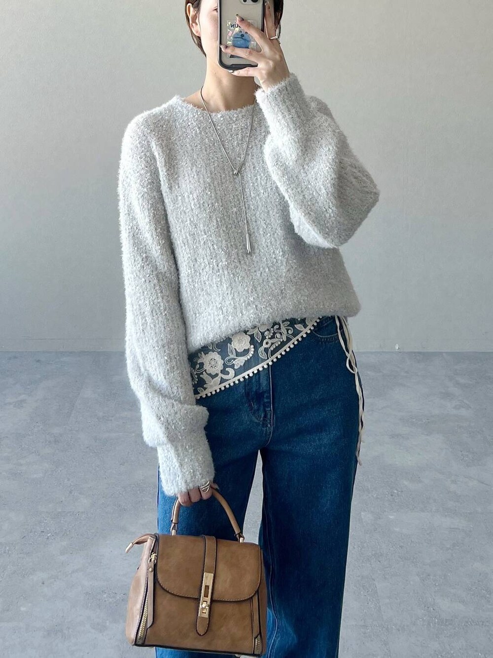 ブルー系のデニムパンツ、ブラウン系のショルダーバッグ、グレー系のニット/セーターを着用したレディースの冬コーディネートの4枚目の写真