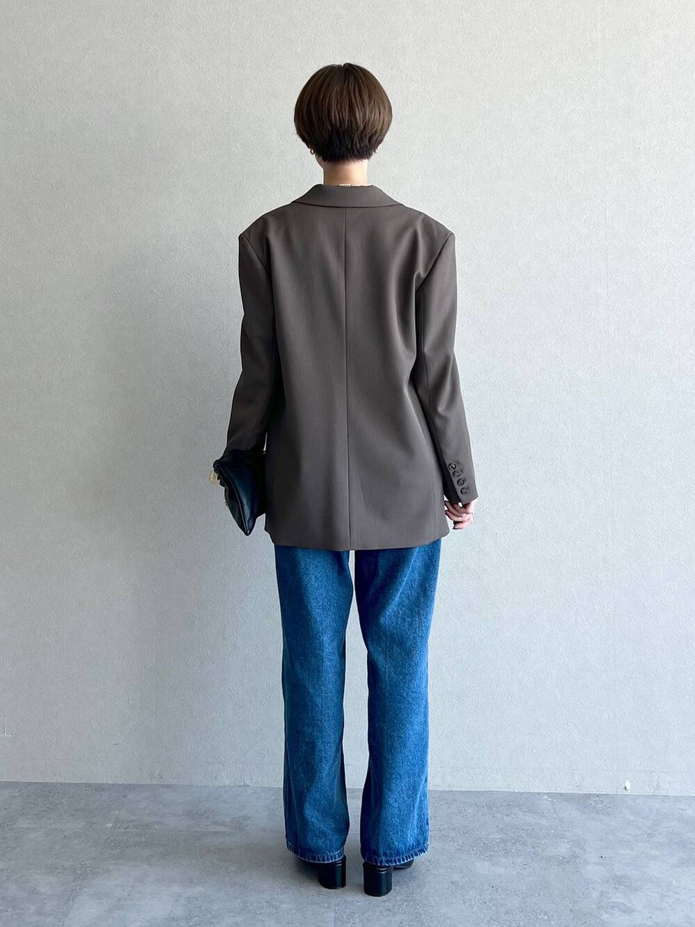 ブラック系のハンドバッグ、ブラウン系のテーラードジャケット、ブルー系のデニムパンツを着用したレディースの秋コーディネートの3枚目の写真