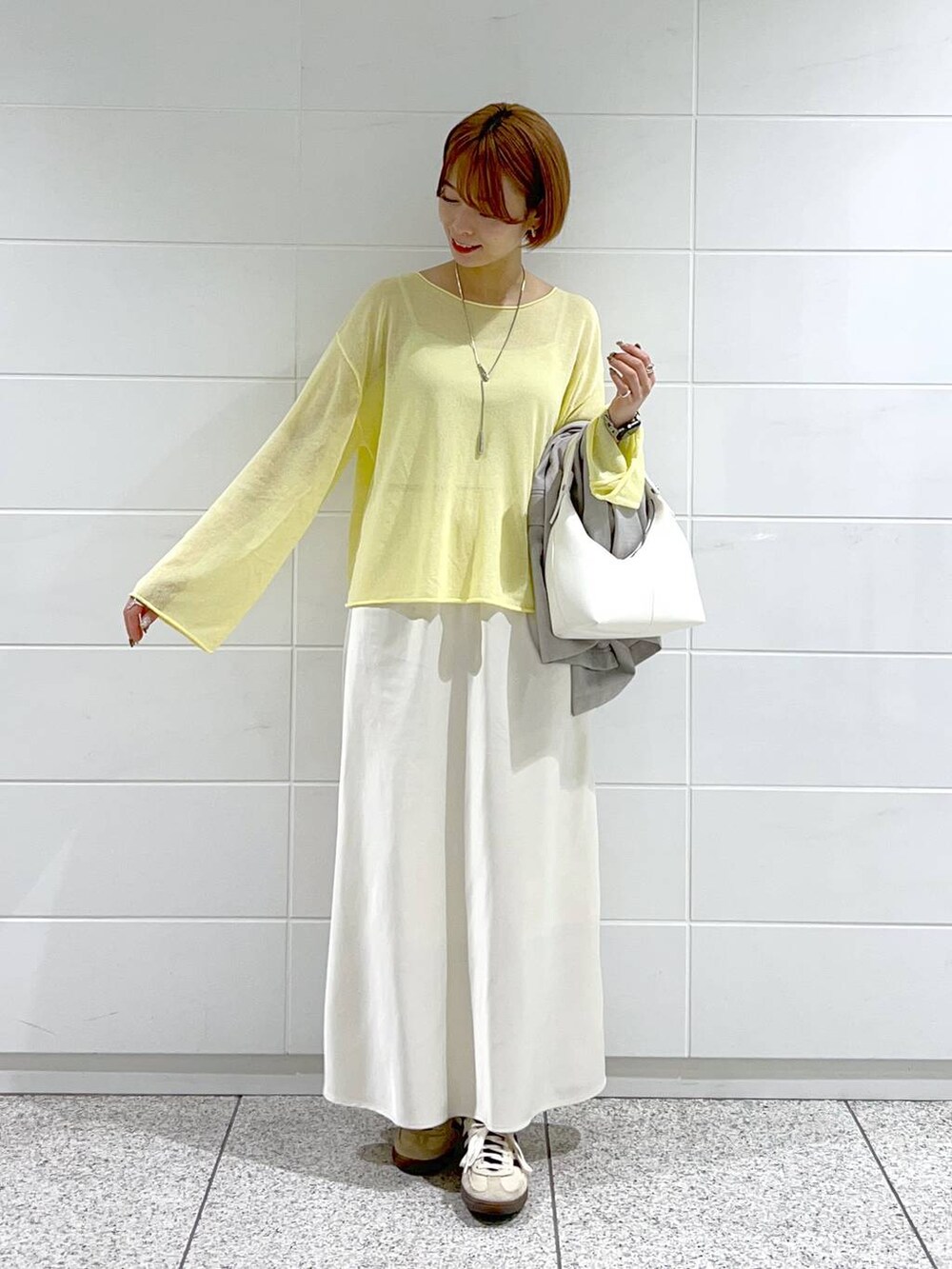 イエロー系のニット/セーター、グレー系のテーラードジャケット、ホワイト系のスカートを着用したレディースの春コーディネートの4枚目の写真