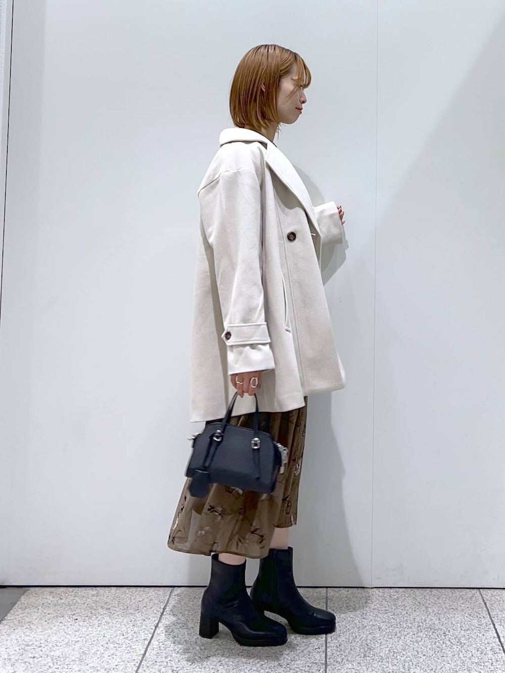 ホワイト系のチェスターコート、ブラック系のボストンバッグ、ブラック系のブーツを着用したレディースの秋コーディネートの2枚目の写真
