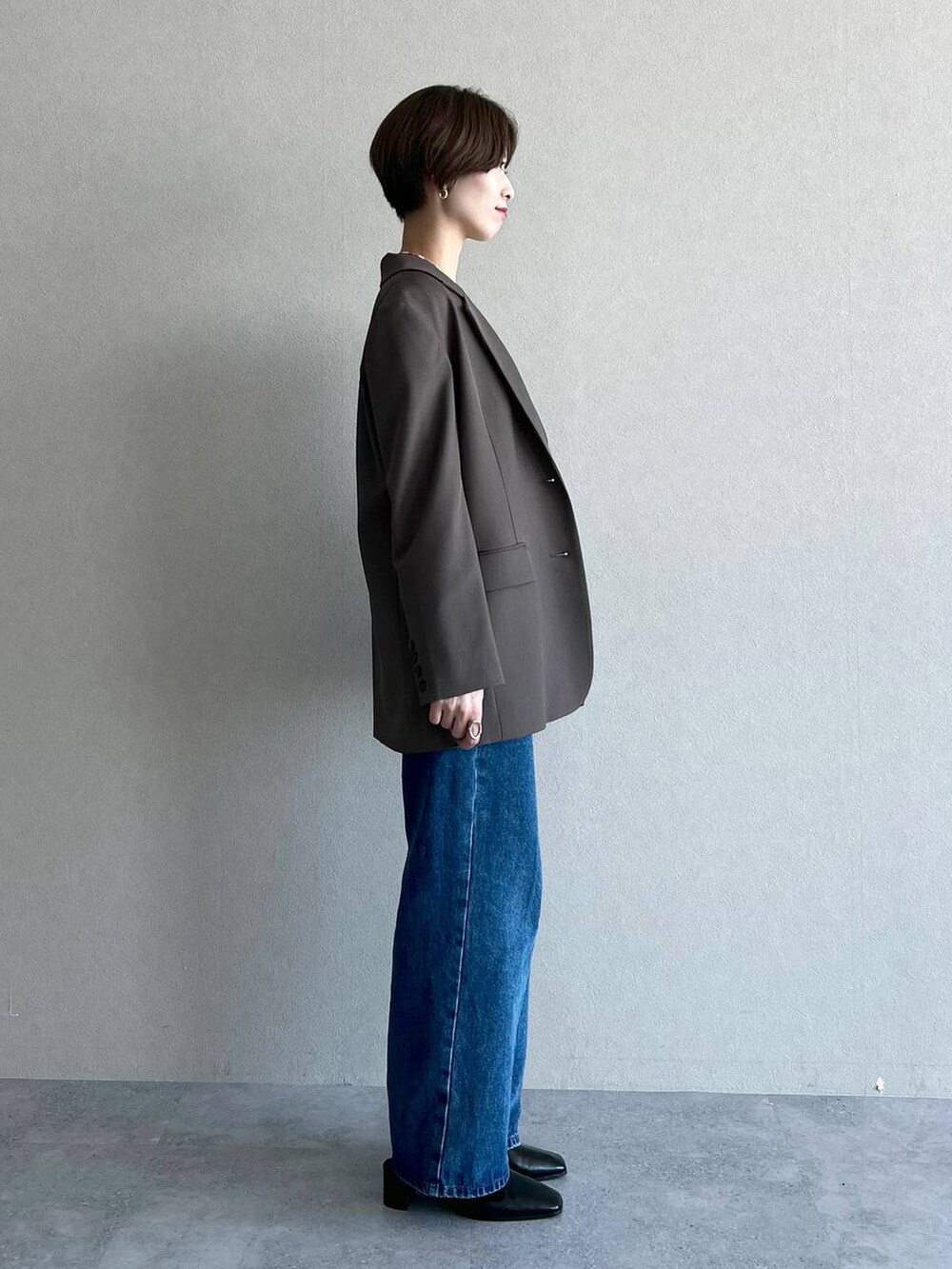 ブラック系のハンドバッグ、ブラウン系のテーラードジャケット、ブルー系のデニムパンツを着用したレディースの秋コーディネートの2枚目の写真