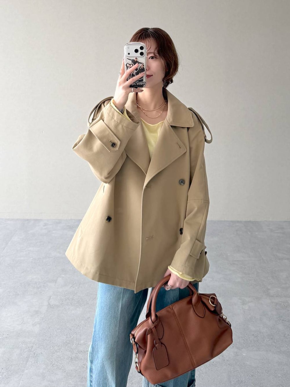 イエロー系のニット/セーター、ブラウン系のボストンバッグ、ベージュ系のトレンチコートを着用したレディースの冬コーディネートの4枚目の写真