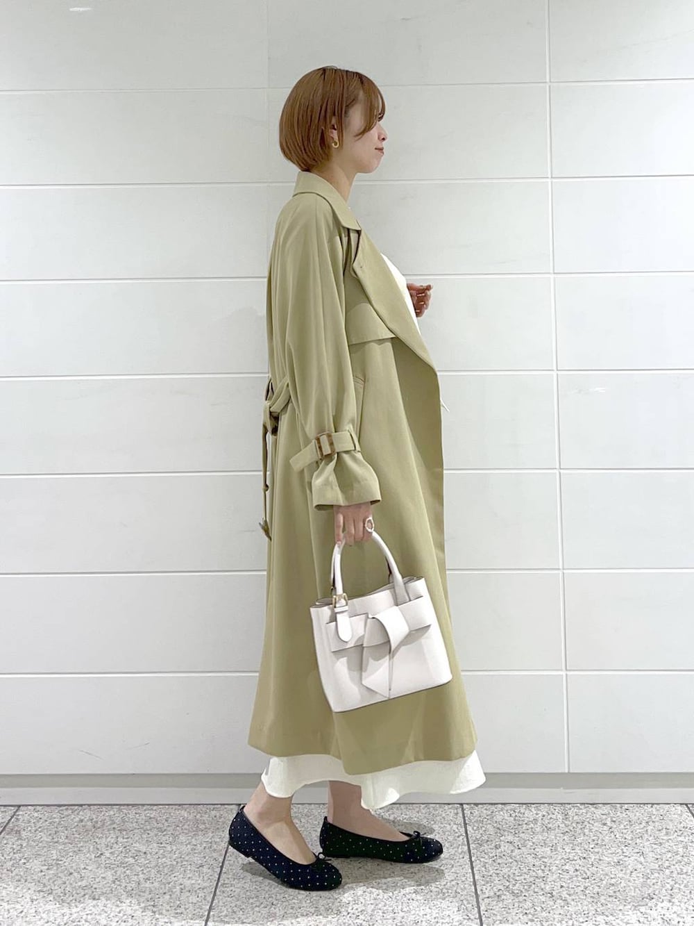 ホワイト系のショルダーバッグ、ベージュ系のトレンチコート、ブラック系のバレエシューズを着用したレディースの春コーディネートの2枚目の写真