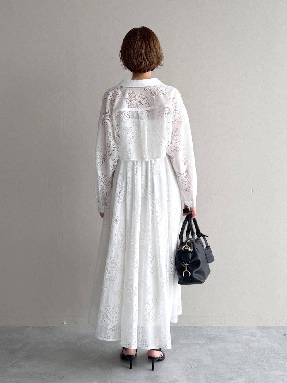 ブラック系のボストンバッグ、ブラック系のサンダル、ホワイト系のワンピースを着用したレディースの春コーディネートの3枚目の写真