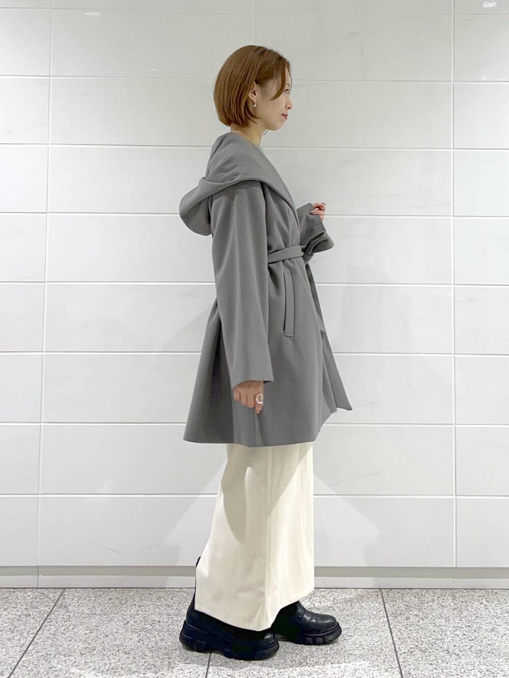 グレー系のノーカラーコート、ブラック系のショルダーバッグ、ブラック系のブーツを着用したレディースの秋コーディネートの2枚目の写真