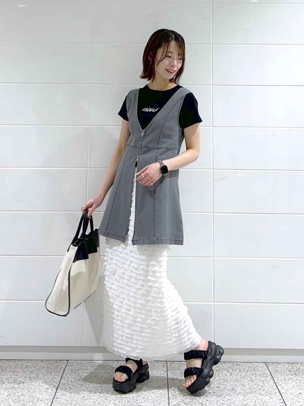 ブラック系のトートバッグ、ブラック系のTシャツ/カットソー、ブラック系のサンダルを着用したレディースの春コーディネートの2枚目の写真