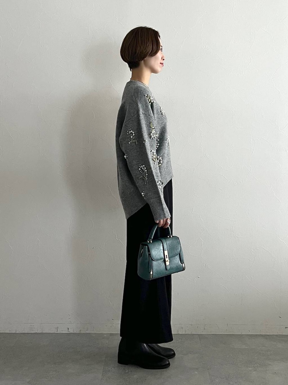 グレー系のニット/セーター、ブラック系のスカート、ブラック系のブーツを着用したレディースの秋コーディネートの2枚目の写真