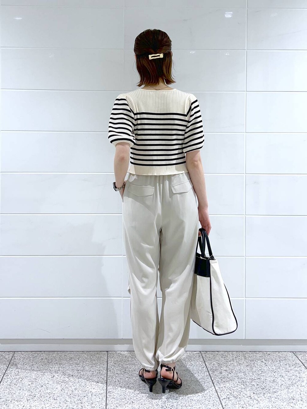 ブラック系のトートバッグ、ブラック系のサンダル、ホワイト系のベストを着用したレディースの春コーディネートの3枚目の写真