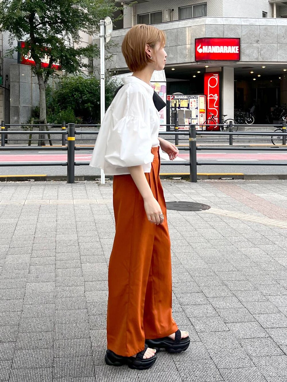 ブラック系のショルダーバッグ、ホワイト系のシャツ/ブラウス、オレンジ系のスラックスを着用したレディースの秋コーディネートの2枚目の写真