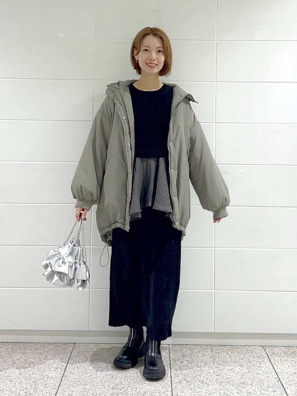 シルバー系のショルダーバッグ、ブラック系のブーツ、ブラック系のスカートを着用したレディースの秋コーディネートの2枚目の写真