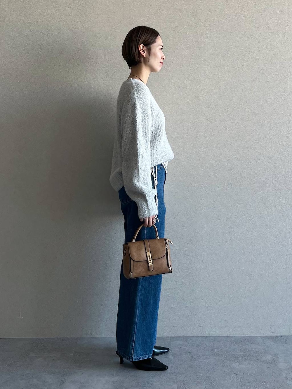 ブルー系のデニムパンツ、ブラウン系のショルダーバッグ、グレー系のニット/セーターを着用したレディースの冬コーディネートの2枚目の写真