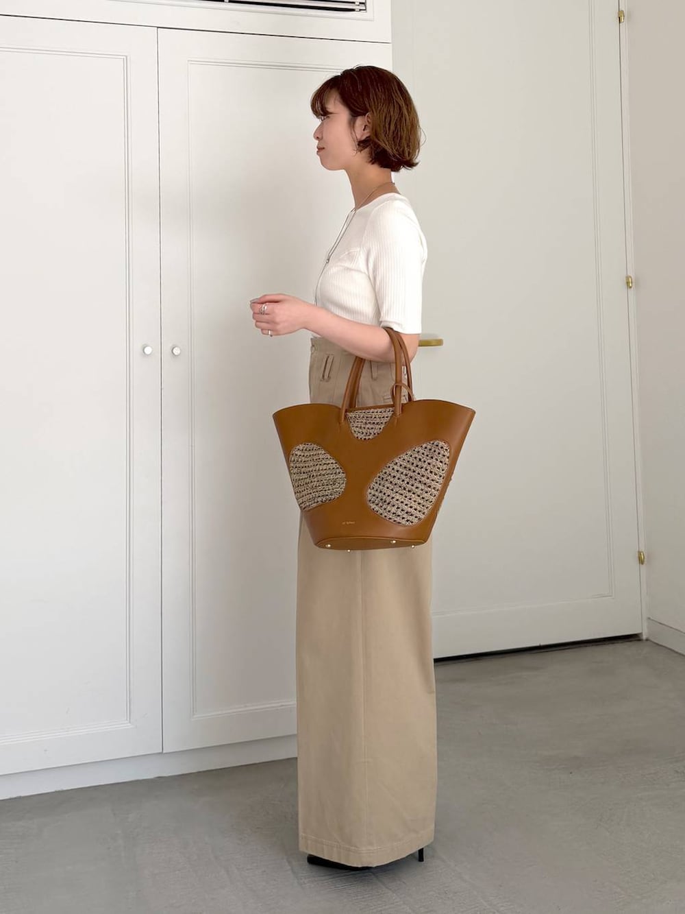 ブラウン系のトートバッグ、ブラック系のサンダル、ホワイト系のTシャツ/カットソーを着用したレディースの春コーディネートの2枚目の写真