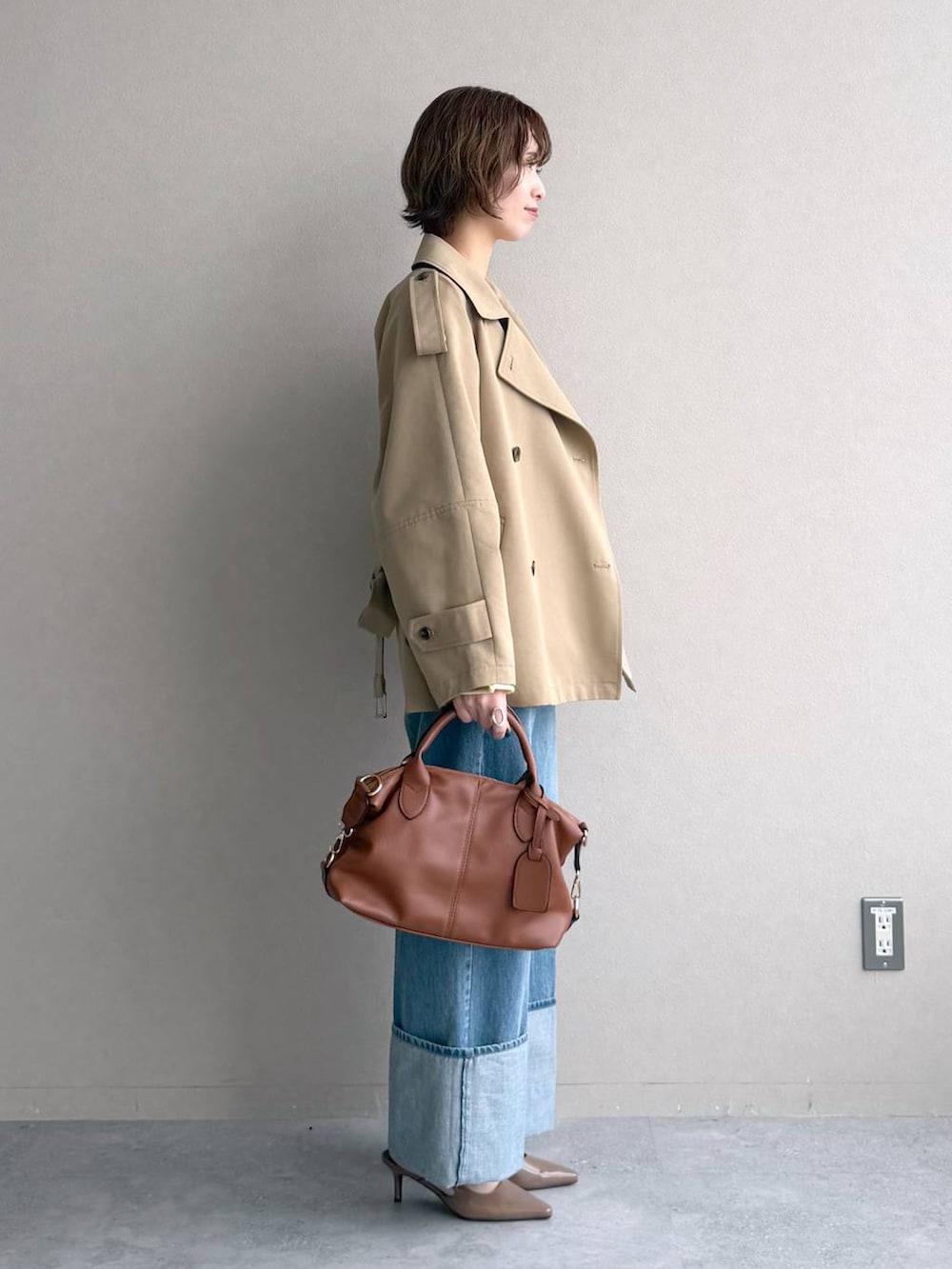 イエロー系のニット/セーター、ブラウン系のボストンバッグ、ベージュ系のトレンチコートを着用したレディースの冬コーディネートの2枚目の写真