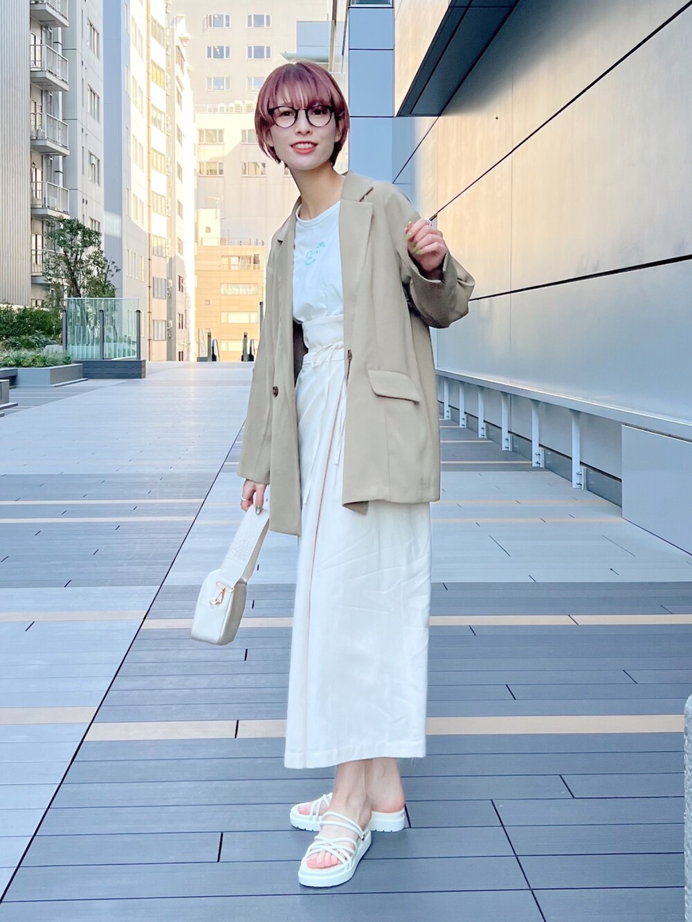 ベージュ系のテーラードジャケット、ホワイト系のスカート、ホワイト系のサンダルを着用したレディースの春コーディネートの2枚目の写真