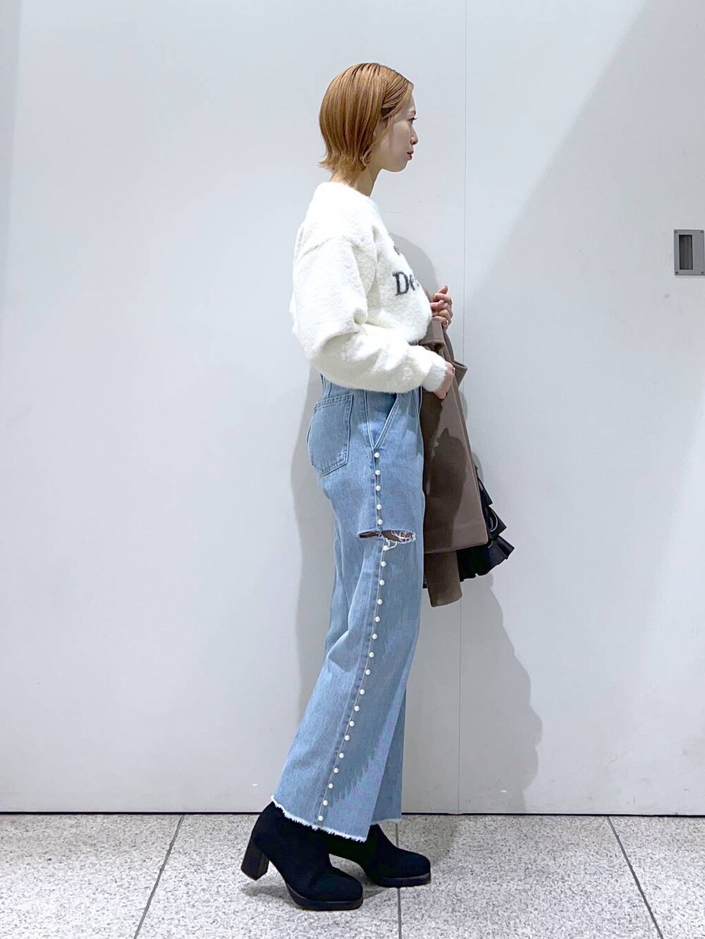 ホワイト系のニット/セーター、ブラウン系のチェスターコート、ブラック系のブーツを着用したレディースの冬コーディネートの5枚目の写真