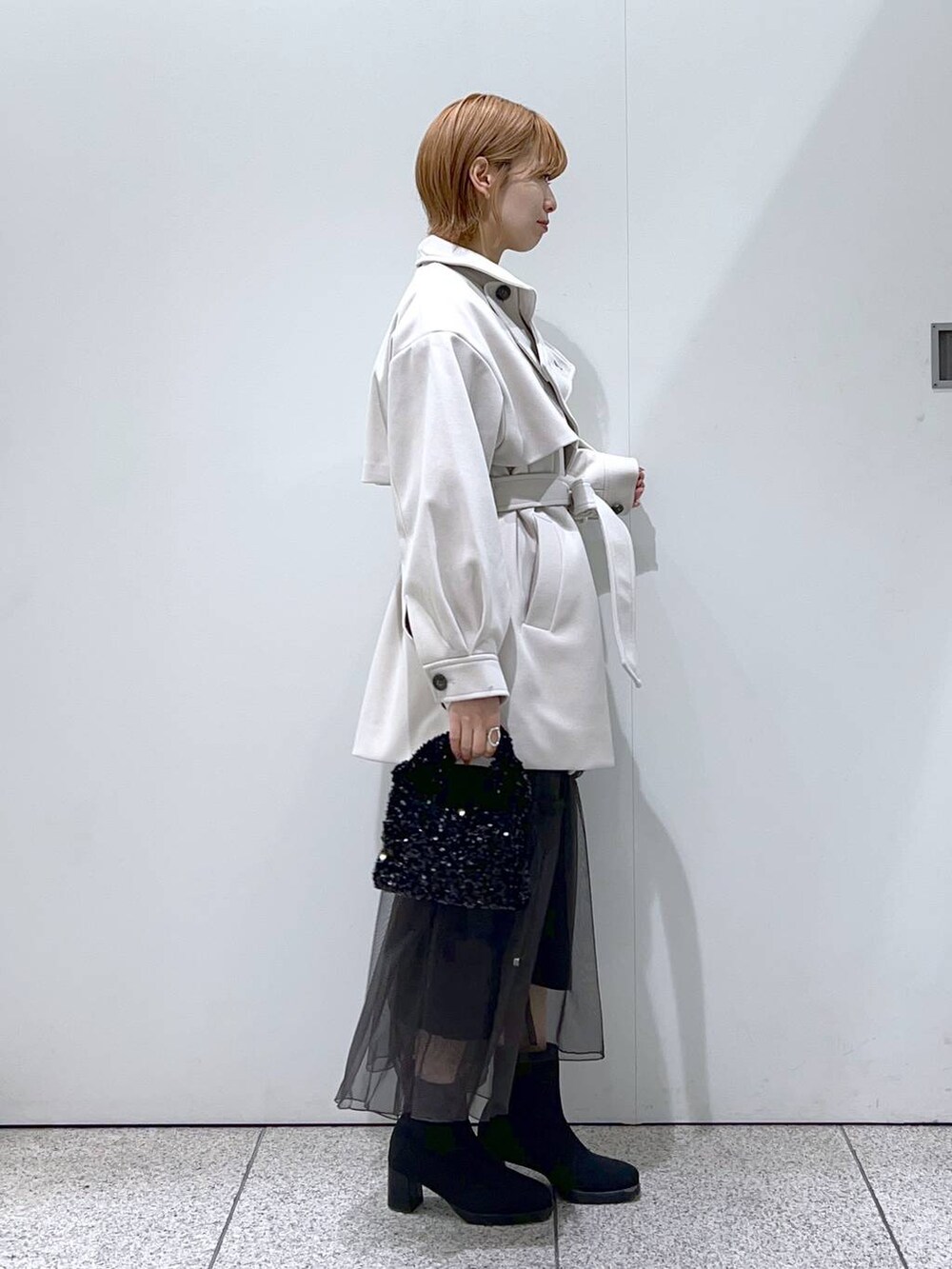 ホワイト系のチェスターコート、ブラック系のブーツ、ブラック系のハンドバッグを着用したレディースの冬コーディネートの2枚目の写真