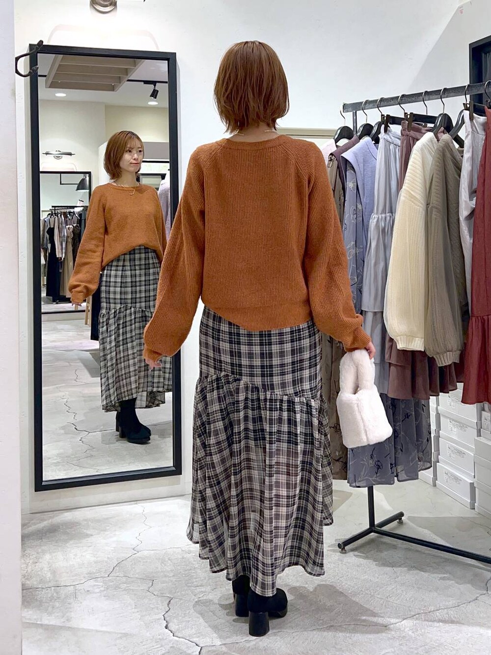 オレンジ系のニット/セーター、ブラック系のブーツ、ホワイト系のスカートを着用したレディースの秋コーディネートの3枚目の写真