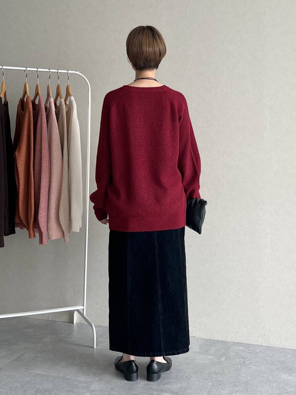 ブラック系のハンドバッグ、ブラック系のスカート、レッド系のニット/セーターを着用したレディースの秋コーディネートの3枚目の写真