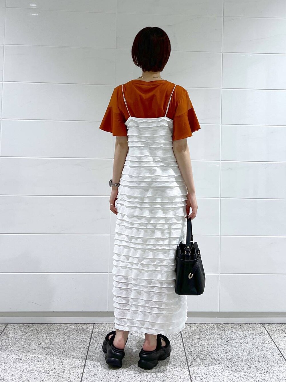 オレンジ系のTシャツ/カットソー、ホワイト系のワンピース、ブラック系のサンダルを着用したレディースの夏コーディネートの3枚目の写真