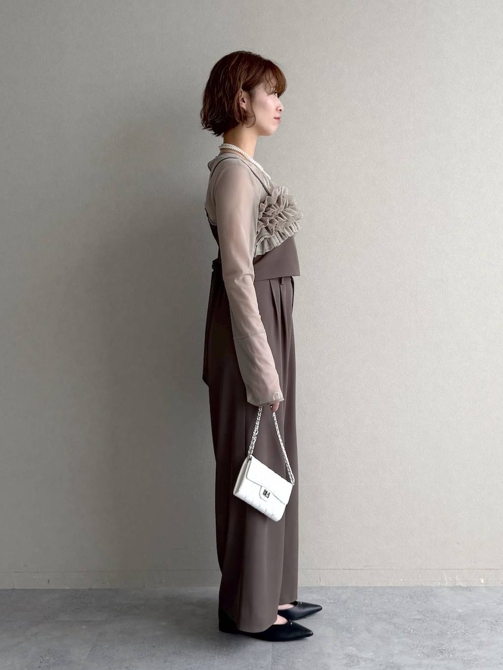 ブラック系のパンプス、ホワイト系のショルダーバッグ、ベージュ系のパンツドレスを着用したレディースの春コーディネートの3枚目の写真