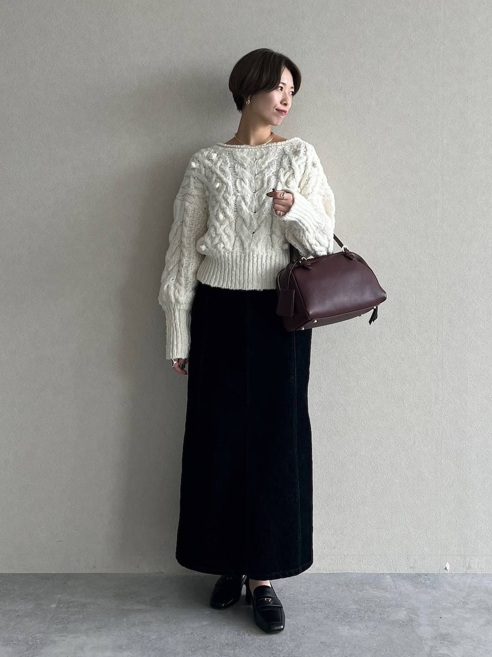 レッド系のハンドバッグ、ブラック系のスカート、ブラック系のローファーを着用したレディースの秋コーディネートの4枚目の写真