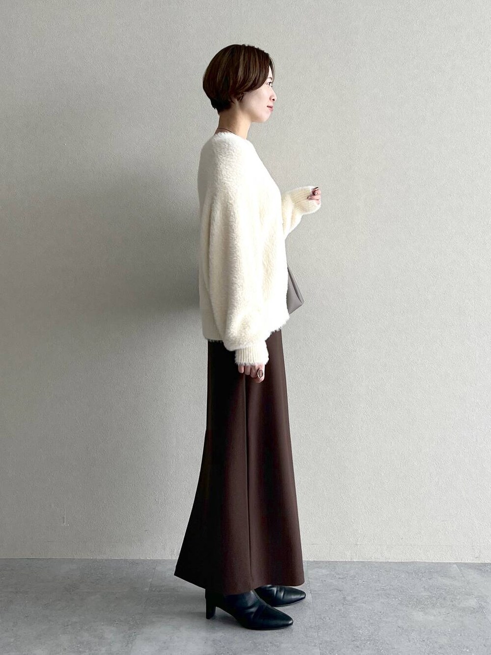 ベージュ系のショルダーバッグ、ブラウン系のスカート、ブラック系のブーツを着用したレディースの秋コーディネートの2枚目の写真