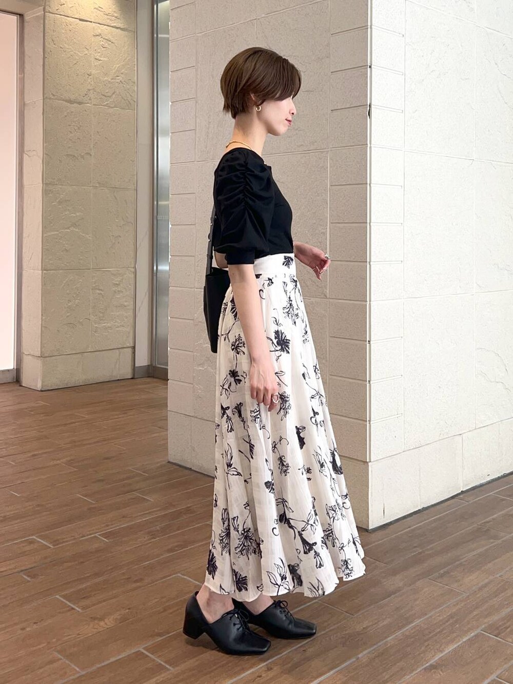 ブラック系のショルダーバッグ、ブラック系のTシャツ/カットソー、ホワイト系のスカートを着用したレディースの夏コーディネートの2枚目の写真