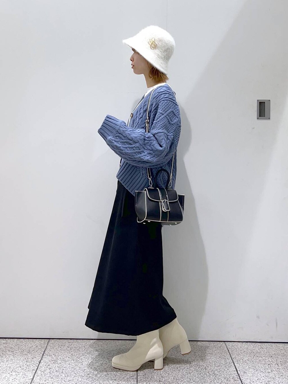 ブラック系のハンドバッグ、ホワイト系のブーツ、ブルー系のカーディガン/ボレロを着用したレディースの秋コーディネートの2枚目の写真