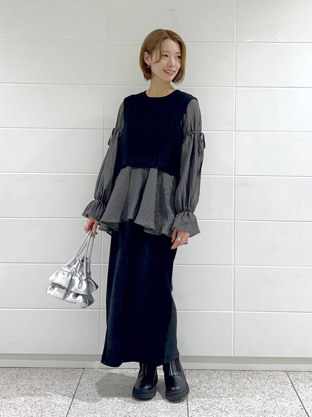 シルバー系のショルダーバッグ、ブラック系のブーツ、ブラック系のスカートを着用したレディースの秋コーディネートの5枚目の写真