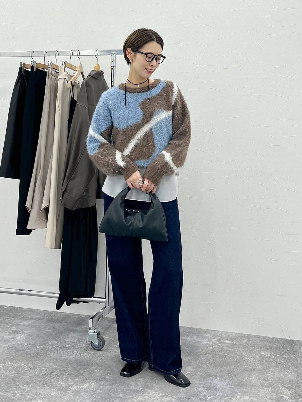 ブラウン系のニット/セーター、ブラック系のハンドバッグ、ブルー系のデニムパンツを着用したレディースの秋コーディネートの2枚目の写真