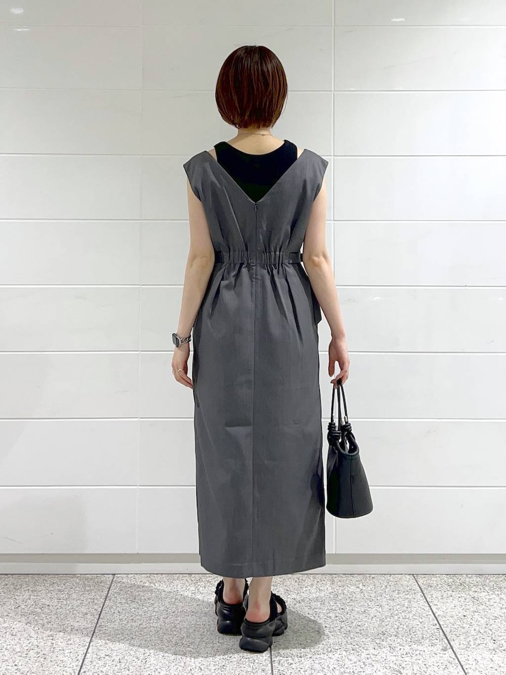 ブラック系のハンドバッグ、ブラック系のサンダル、グレー系のジャンパースカートを着用したレディースの夏コーディネートの3枚目の写真