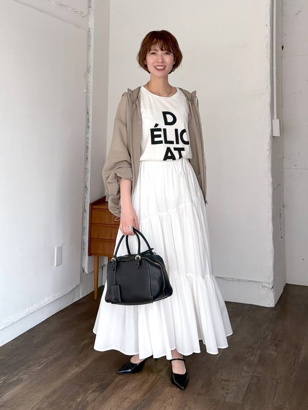 ブラック系のハンドバッグ、ブラック系のサンダル、ホワイト系のスカートを着用したレディースの春コーディネートの7枚目の写真