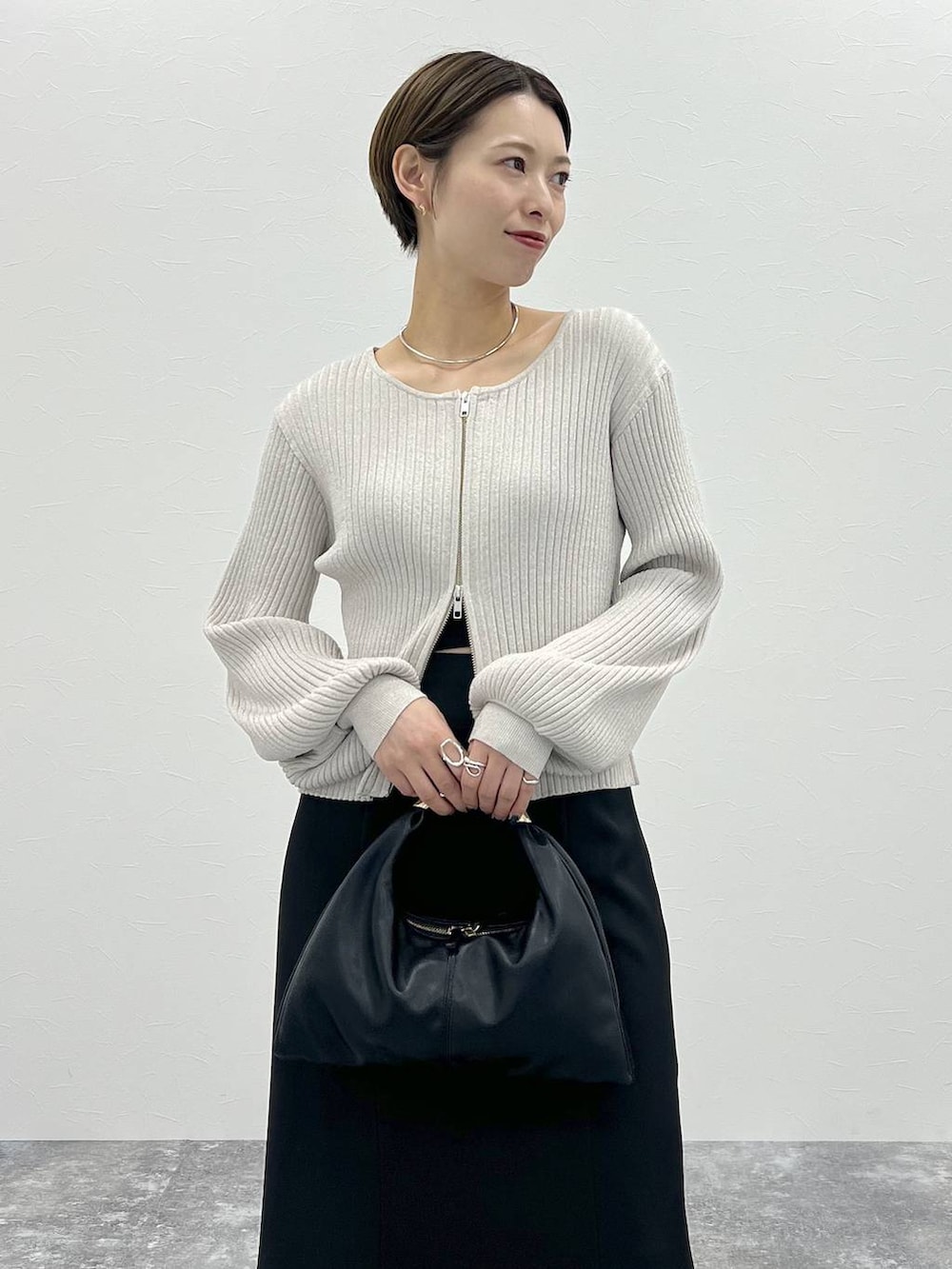 ブラック系のスカート、ブラック系のハンドバッグ、ホワイト系のカーディガン/ボレロを着用したレディースの秋コーディネートの4枚目の写真