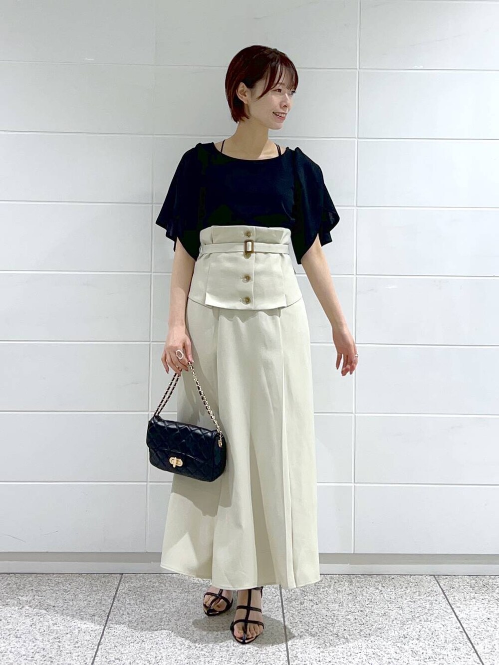 ホワイト系のスカート、ブラック系のショルダーバッグ、ブラック系のサンダルを着用したレディースの夏コーディネートの2枚目の写真