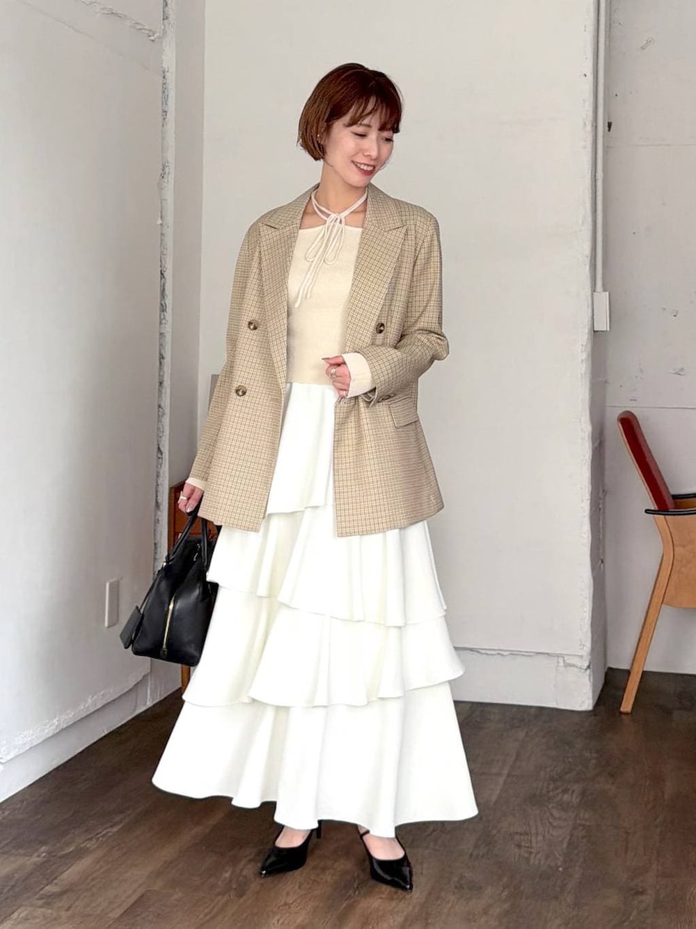 ブラック系のハンドバッグ、ベージュ系のテーラードジャケット、ホワイト系のスカートを着用したレディースの春コーディネートの4枚目の写真