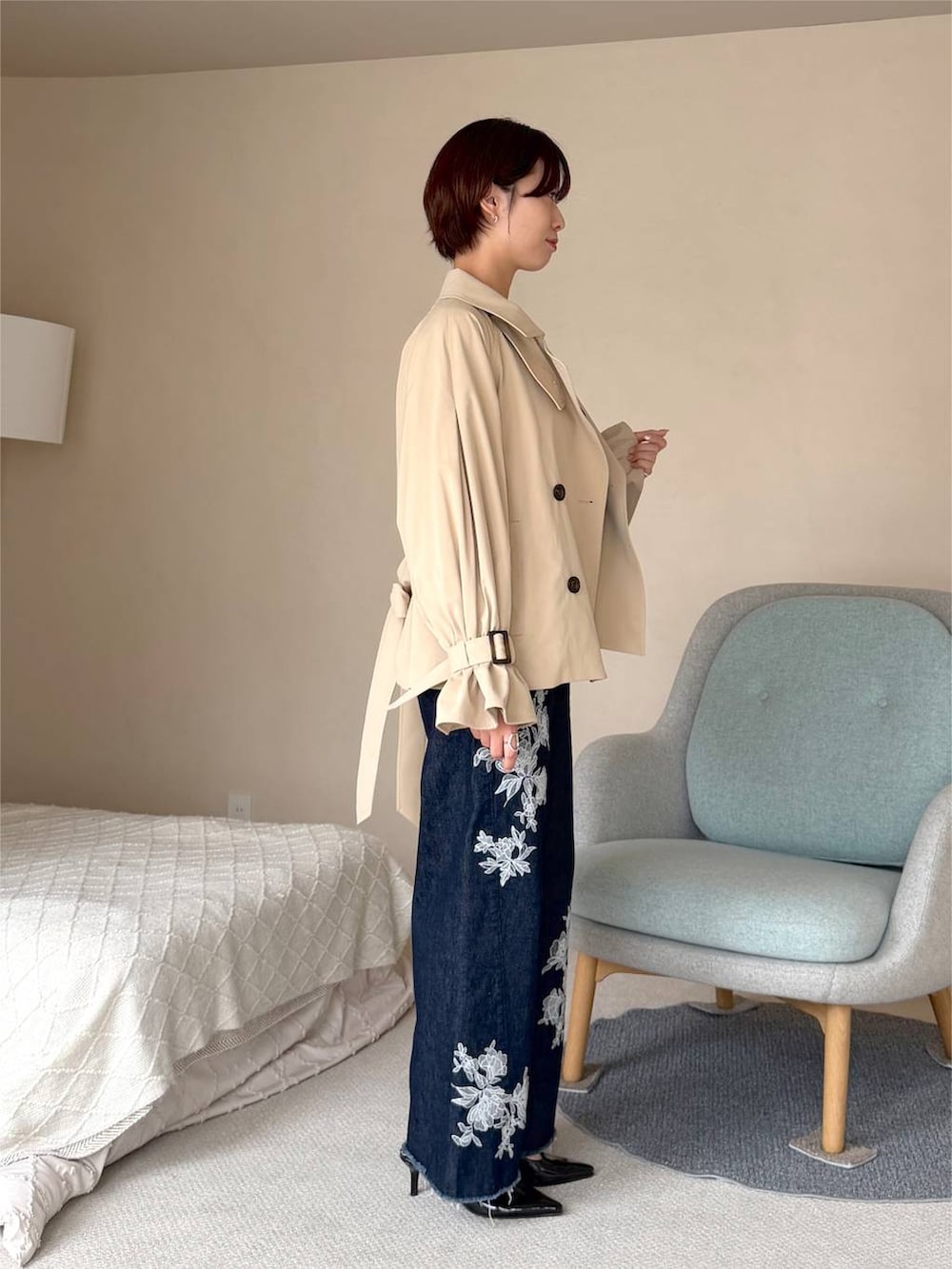 ブルー系のデニムパンツ、ベージュ系のトレンチコート、ブラック系のハンドバッグを着用したレディースの秋コーディネートの2枚目の写真