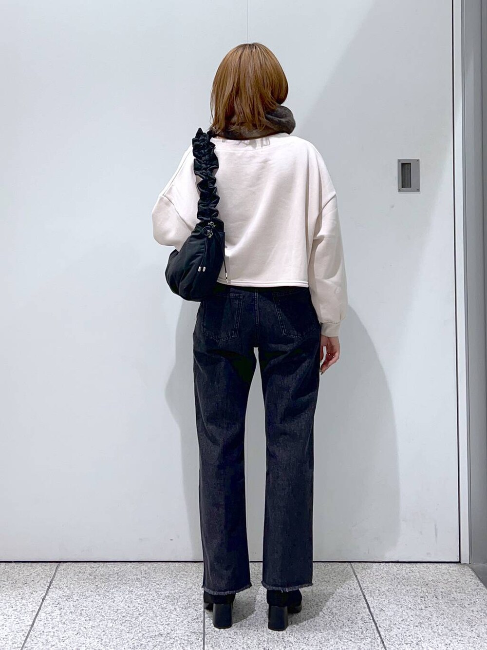 ブルー系のデニムパンツ、ブラック系のハンドバッグ、ブラック系のブーツを着用したレディースの秋コーディネートの3枚目の写真