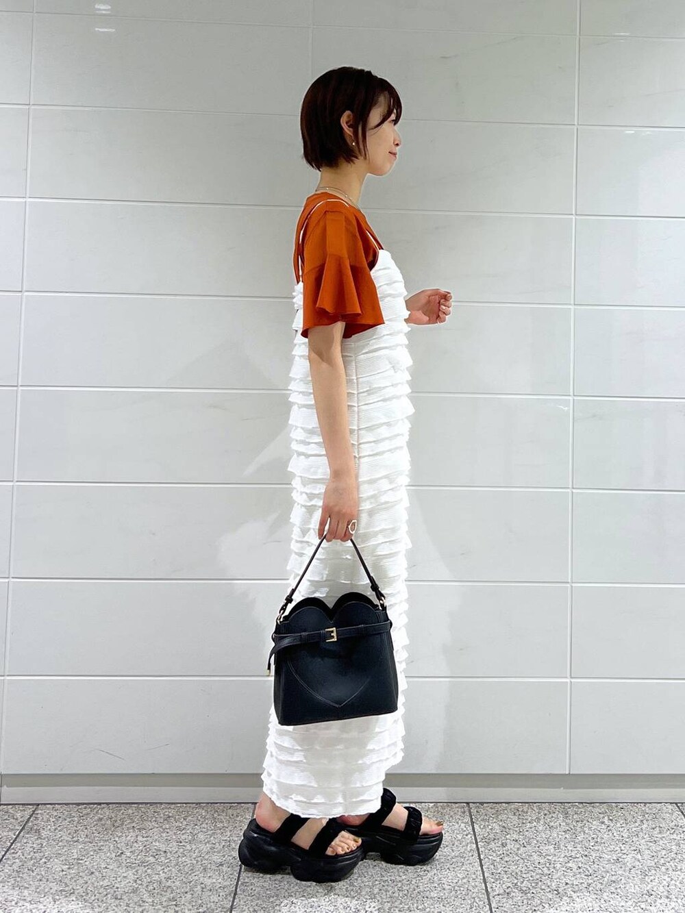 オレンジ系のTシャツ/カットソー、ホワイト系のワンピース、ブラック系のサンダルを着用したレディースの夏コーディネートの2枚目の写真