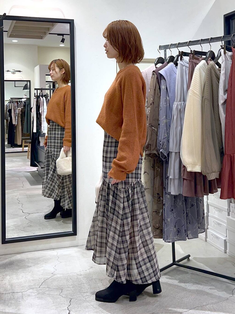 オレンジ系のニット/セーター、ブラック系のブーツ、ホワイト系のスカートを着用したレディースの秋コーディネートの2枚目の写真