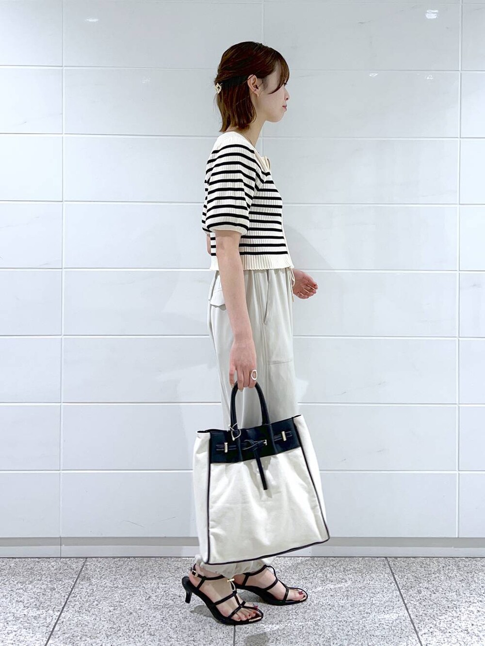 ブラック系のトートバッグ、ブラック系のサンダル、ホワイト系のベストを着用したレディースの春コーディネートの2枚目の写真