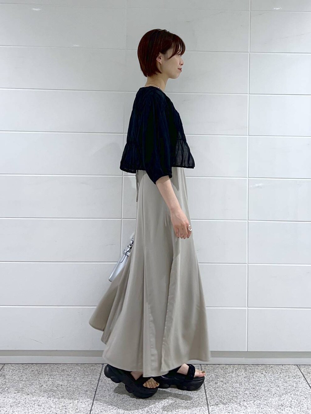 ブラック系のブルゾン、シルバー系のショルダーバッグ、ベージュ系のワンピースを着用したレディースの夏コーディネートの2枚目の写真