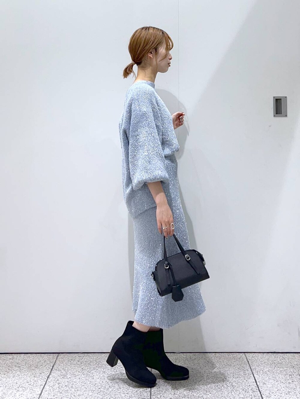 ブラック系のボストンバッグ、ブラック系のブーツ、ブルー系のニット/セーターを着用したレディースの秋コーディネートの2枚目の写真