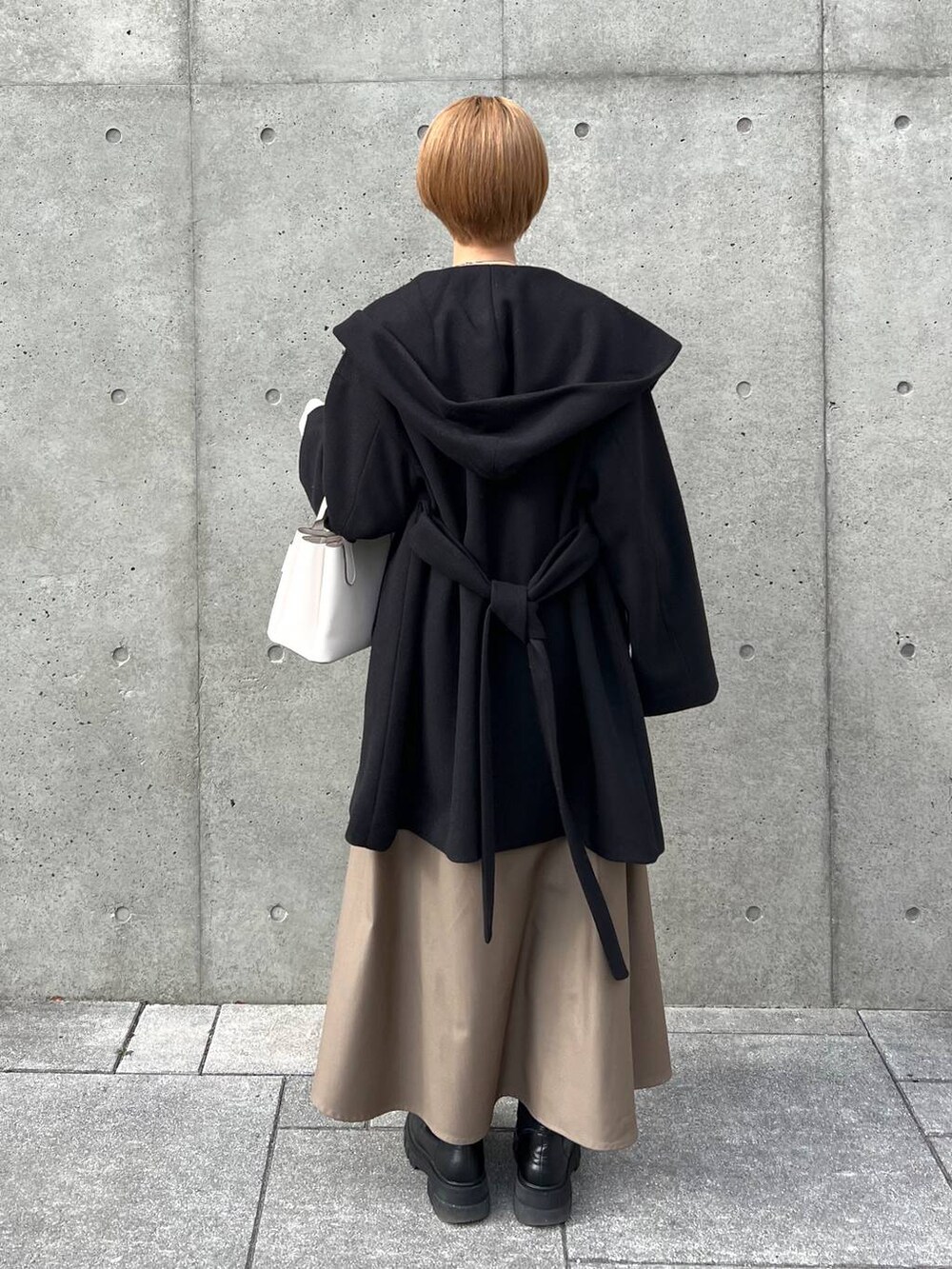 ブラック系のノーカラーコート、ブラック系のブーツ、ホワイト系のショルダーバッグを着用したレディースの冬コーディネートの3枚目の写真