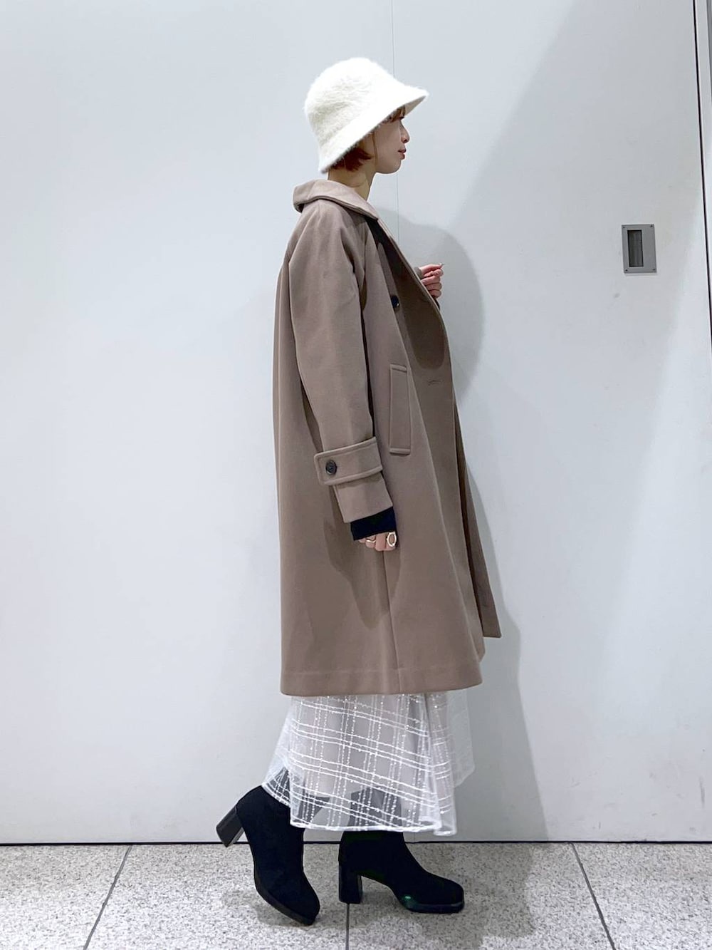 ブラウン系のチェスターコート、ブラック系のブーツ、ブラック系のニット/セーターを着用したレディースの冬コーディネートの2枚目の写真