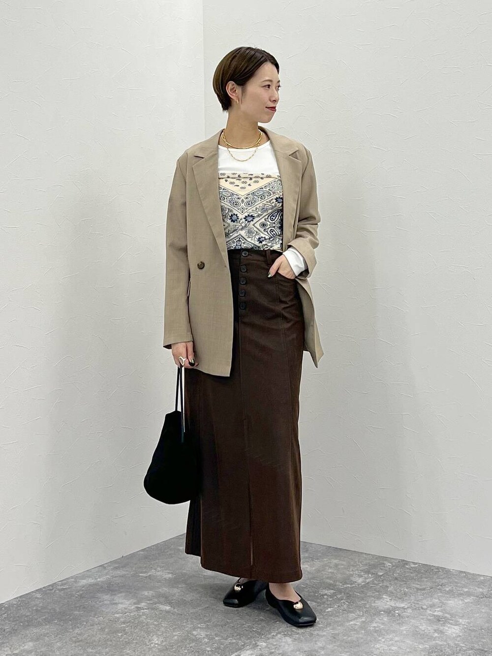 ベージュ系のテーラードジャケット、ホワイト系のTシャツ/カットソー、ブラウン系のスカートを着用したレディースの秋コーディネートの2枚目の写真