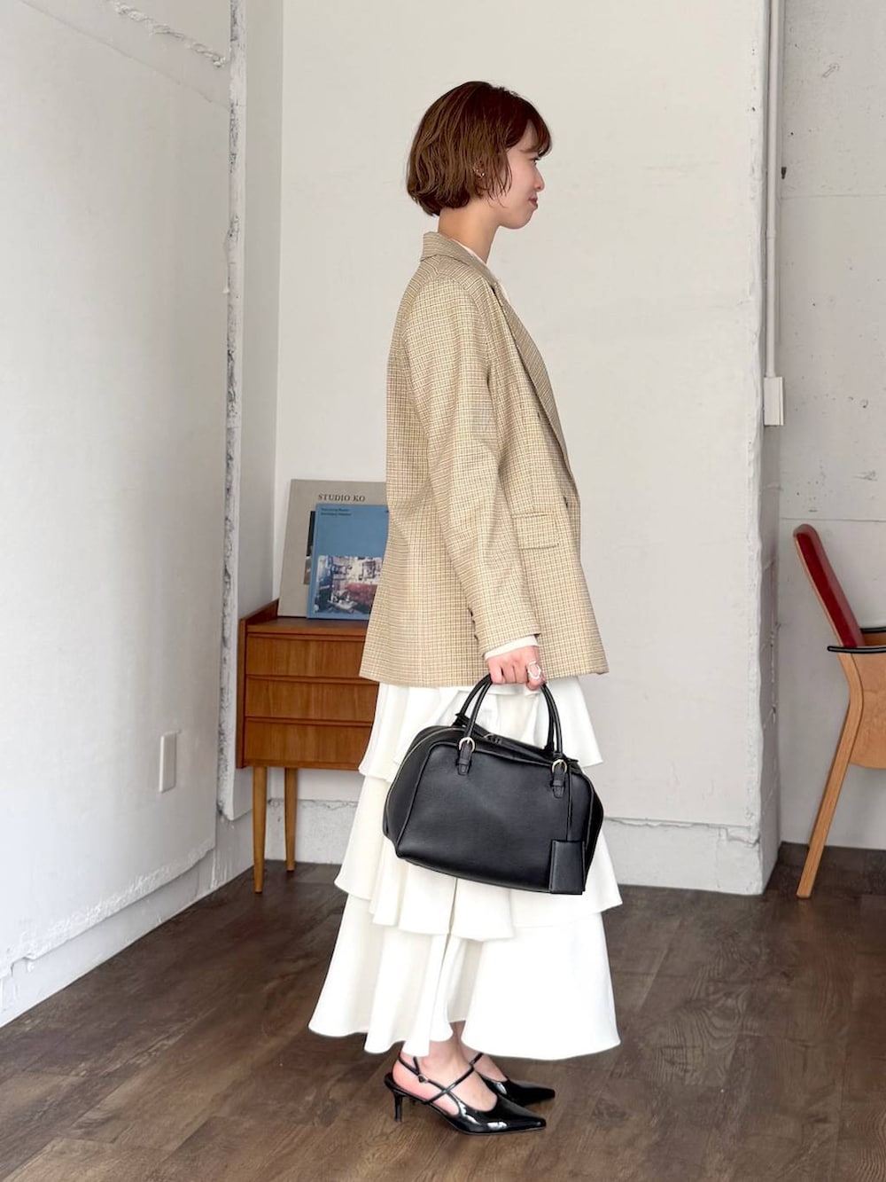 ブラック系のハンドバッグ、ベージュ系のテーラードジャケット、ホワイト系のスカートを着用したレディースの春コーディネートの2枚目の写真