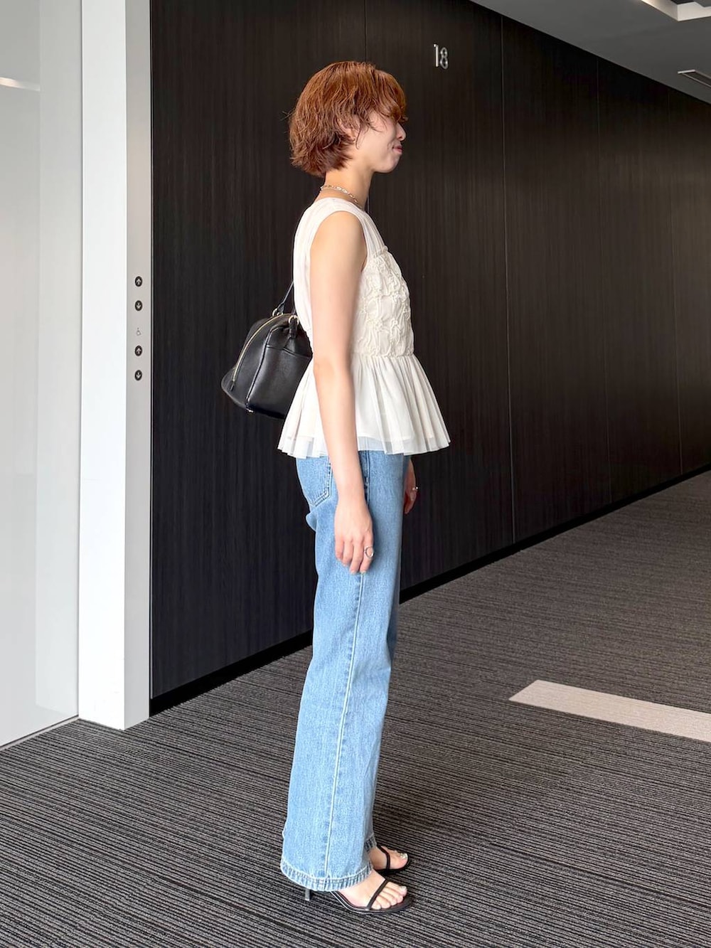 ブラック系のハンドバッグ、ブルー系のデニムパンツを着用したレディースの夏コーディネートの2枚目の写真