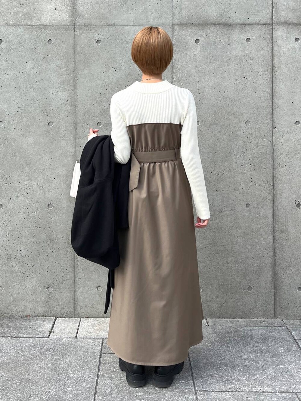 ブラック系のノーカラーコート、ブラック系のブーツ、ホワイト系のショルダーバッグを着用したレディースの冬コーディネートの6枚目の写真